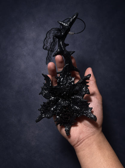 Thorn Bloom Talisman resting across a hand, showing its thorned stem, layered black bloom and lace.