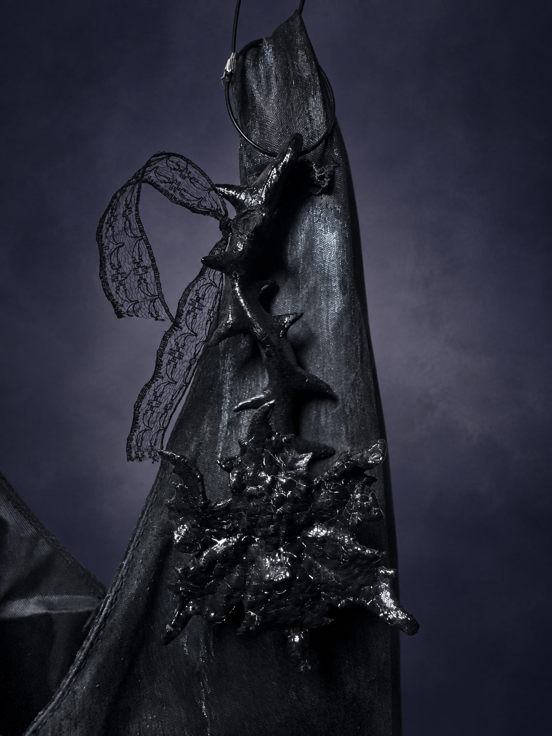 Thorn Bloom Talisman hanging from a dark bag, showing the attachment loop and trailing black lace.